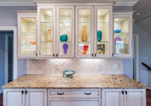 Glass kitchen cabinets from Houston glass company with multi-colored vases displayed inside